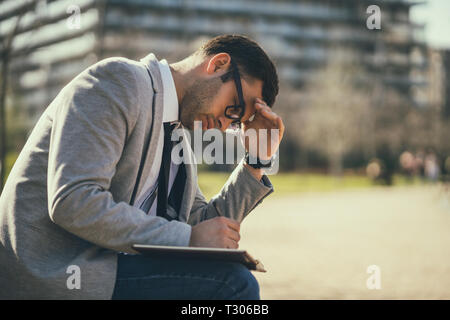 Young businessman is sitting in park and making plans. Stock Photo