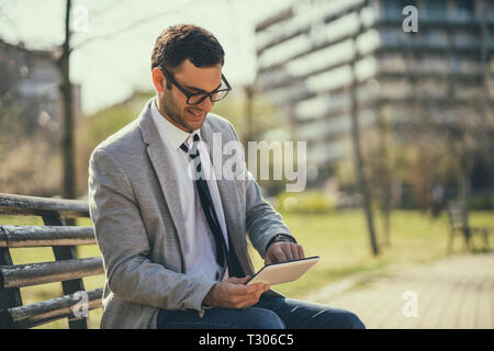 Young happy businessman is using digital tablet in park. Stock Photo