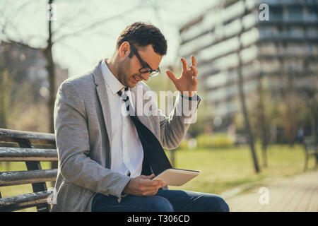 Young businessman is using digital tablet in park. He is angry. Stock Photo