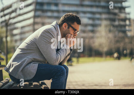 Young businessman is sitting in park after being fired. He is depressed. Stock Photo