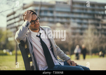 Young businessman is very tired. He is sitting in park after work. Stock Photo