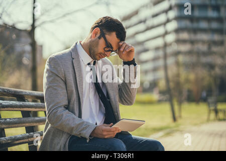 Young businessman is using digital tablet in park. He is angry. Stock Photo