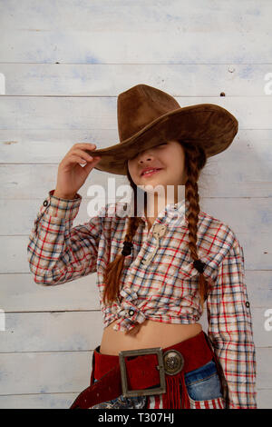 Little girl in a wide-brimmed cowboy hat and traditional dress posing on a light wooden background Stock Photo