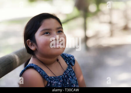 Cute 8 year old girl of mixed ethnicity, staring into the sky with a thoughtful look and dressed in traditional country western clothes. Stock Photo