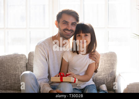 Father and daughter with gift box sitting on couch Stock Photo