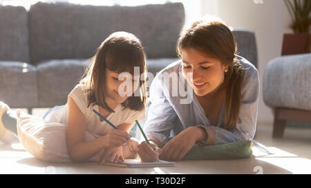 Mother drawing with daughter lying on warm floor Stock Photo