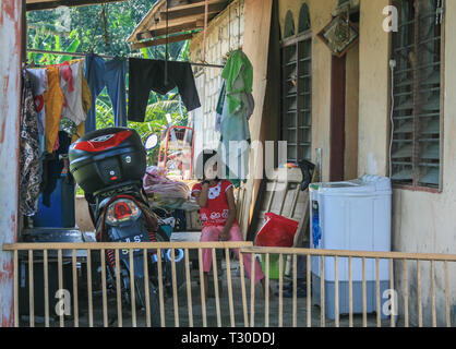 Young girl sitting outside her home in Kampung Sungai Melayu, Iskandar Puteri, Johor, Malaysia Stock Photo