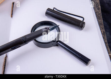 Magnifying glass with fountain pen on an empty notebook Stock Photo