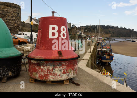 Red, port navigation buoy, lateral mark on quayside for maintenance, with fishing boat moored towall quayside at low tide in Conwy north wales uk Stock Photo