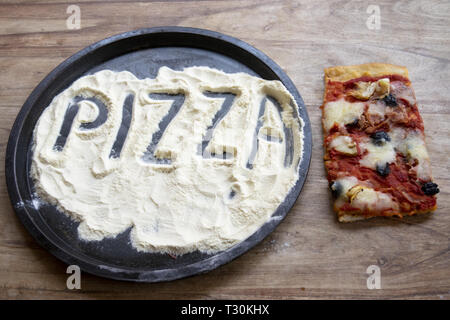 pizza word written on the flour contained in a baking tin with near a piece of capricciosa Stock Photo