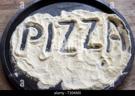 pizza word written on the flour contained in a baking tin Stock Photo