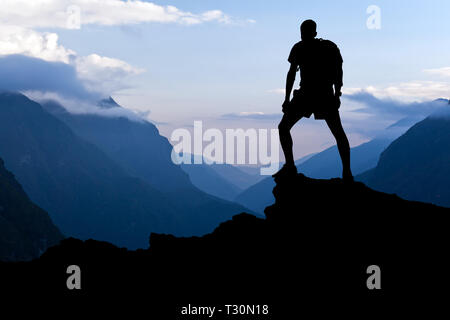 Man on successful hiking, silhouette in mountains. Hiker on top of mountain looking at beautiful Himalayan landscape on sunset, Nepal. Stock Photo