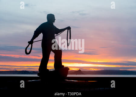Newlyn, Cornwall, UK. 5th Apr, 2019. UK Weather. A cold but calm and colourful start to the morning at Newlyn looking out to Mounts Bay. Seen here Tom Leapers bronze memorial statue to Newlyn Fishermen silhoutted against the sunrise. Credit: Simon Maycock/Alamy Live News Stock Photo