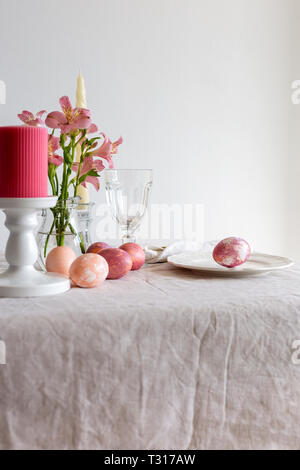 Table setting for Easter meal with flowers and candles. Easter table set on linen tablecloth with Easter egg on plate with decor. Concept of holiday t Stock Photo