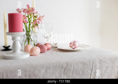 Table setting for Easter meal with flowers and candles. Easter table set on linen tablecloth with Easter egg on plate with decor. Concept of holiday t Stock Photo