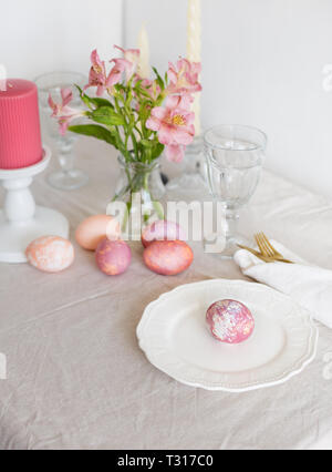 Beautiful festive Easter table setting with linen napkin and Alstroemeria flowers, pink candles, painted Easter eggs. Concept of Easter breakfast Stock Photo