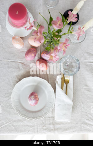 Bright festive Easter table setting with linen tablecloth, golden fork and knife, painted eggs and flowers. Top view flat lay, concept of Easter festi Stock Photo