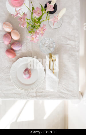 Beautiful festive Easter table setting with linen tablecloth, golden fork and knife, painted eggs and flowers. Top view flat lay, concept of Easter fe Stock Photo