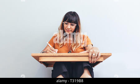 Portrait of a woman sitting on floor with a drawing pad making a sketch. Close up of a creative artist at work drawing a sketch. Stock Photo