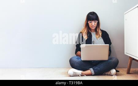 Female freelancer working on laptop sitting on floor. Woman using a laptop computer working from home. Stock Photo