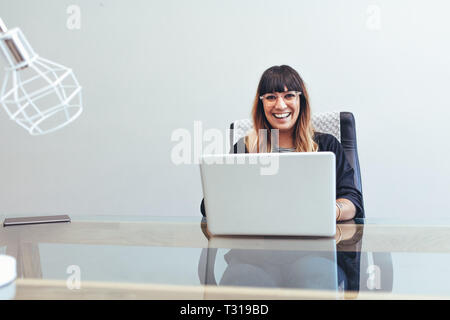 Portrait of a smiling woman entrepreneur sitting at her desk in office working on laptop. Businesswoman in office working on laptop. Stock Photo