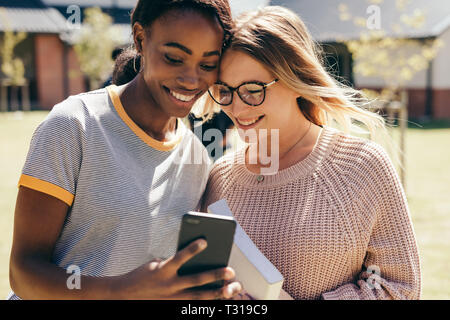Young women taking selfie with mobile phone at university during break. Two high school girls with mobile phone outdoors in campus.
