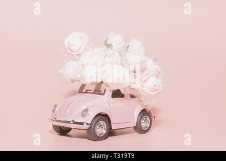 Petrozavodsk, Russia - April 04, 2019: Pink retro toy car with bouquet of white Roses on pink background. Concept Valentine's day, February 14 card, 8 Stock Photo