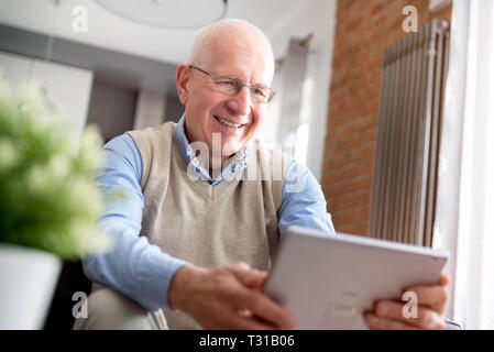 Elderly man using tablet PC. Senior sitting on sofa in living room Stock Photo