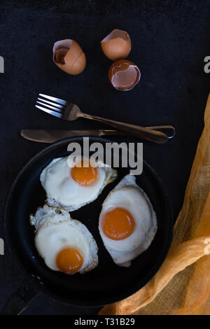 Overhead view of  fried eggs in black baking pan on dark background Stock Photo