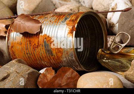 Still life of a rusty empty used tin can with lid and pull waste on pebble beach floor as an environmental pollution closeup Stock Photo