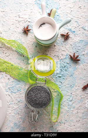 Vertical photo with top view on glass jar with sealed opened cover. Jar is full of raw poppy seeds. Jar is placed on light blue and white textured boa Stock Photo