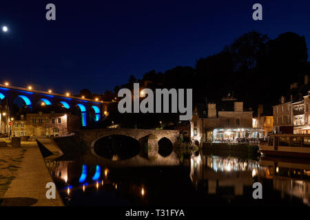 Picturesque viaduct, old stone houses and restaurants of Dinan port reflected in the water at night. Beautiful illumination under a starry sky. Stock Photo