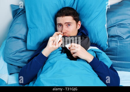 Photo of sick man using nasal spray while lying in bed Stock Photo