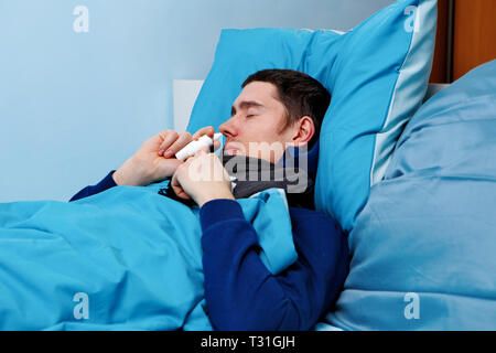 Image of sick man using nasal spray while lying in bed Stock Photo