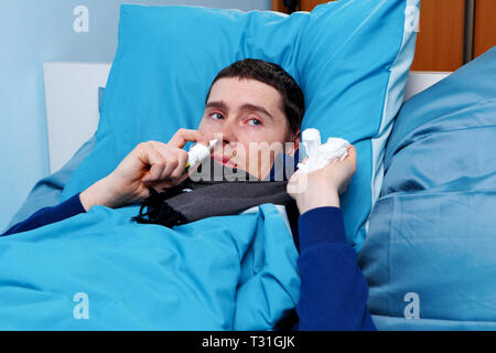 Image of sick man using nasal spray while lying in bed Stock Photo