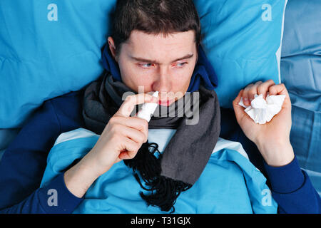Sick brunet man using nasal spray while lying in bed Stock Photo
