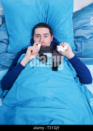 Sick brunet man using nasal spray while lying in bed Stock Photo
