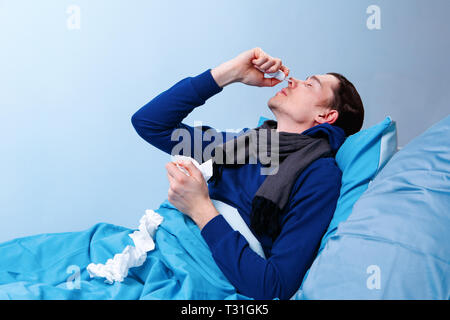 Sick brunet man using nasal spray while lying in bed. Stock Photo