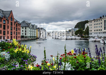 View of boats and buildings in an Alesund town center marina with colourful flowers in the foreground. Stock Photo