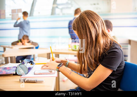 Young girl writing a test in school with other kids at day Stock Photo