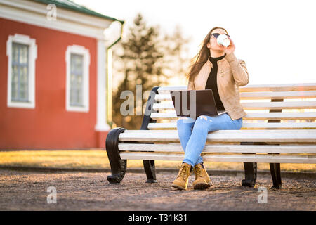 Remote work in outdoor office. Business woman working with laptop in the park or student studying outdoors in campus. Lady drinking coffee. Stock Photo