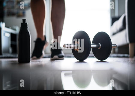 Fitness, home workout and weight training concept. Man starting to exercise with dumbbell. Water or protein shake bottle on floor. Stock Photo