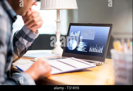 Man reading business report paper. Laptop with financial graphs, statistics and market progress. Entrepreneur counting budget or income tax. Stock Photo