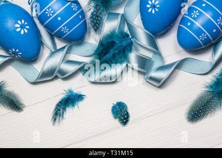 Easter background with blue eggs, feathers and ribbon on white wooden table. Top view with copy space. Stock Photo