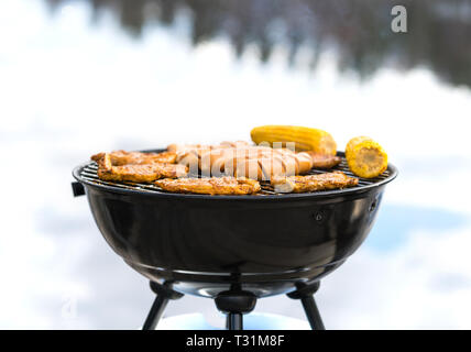 Grilling at the beach. Food cooking on a charcoal kettle grill. Sausages, meat, corn and vegetables in outdoor barbeque in summer. BBQ party. Stock Photo