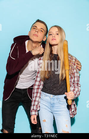 Sport games. Close up fashion portrait of two young cool hipster girl and boy wearing jeans wear. Woman and boy with baseball bat. Studio shot of two serious best friends having fun together. Stock Photo