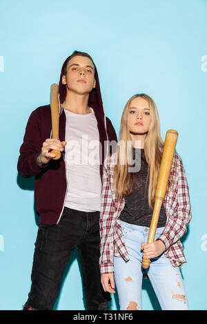 Sport games. Close up fashion portrait of two young cool hipster girl and boy wearing jeans wear. Woman and boy with baseball bat. Studio shot of two serious best friends having fun together. Stock Photo
