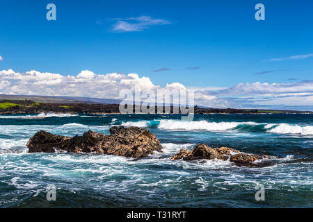 Volcanic rock surrounded by blue ocean, offshore Punaluu Black Sand Beach in Hawaii. Clouds and sky in the background; shoreline in the distance. Stock Photo