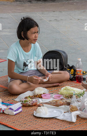 a small girl sitting on a mat or rug in thailand with a picnic of assorted thai food eating alfresco. Stock Photo