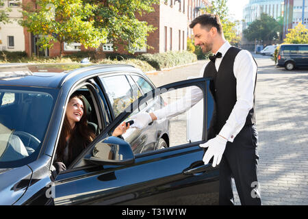 Smiling Young Woman Sitting In Car And Giving Car Key To Valet Stock Photo